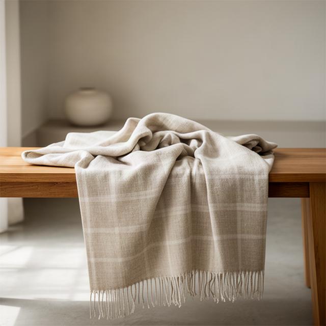 Zacht linnen plaid in zandkleur over een houten bank in een rustige kamer
